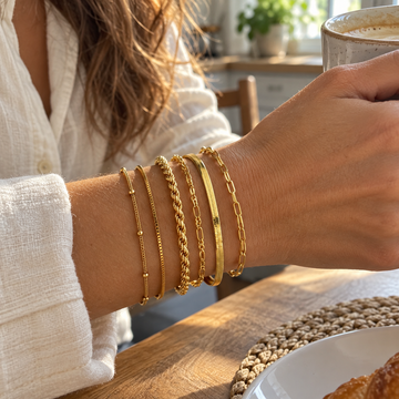 Gold six-chain bracelet stack on an adult wrist beside a morning coffee mug · AI-generated illustrative demo image