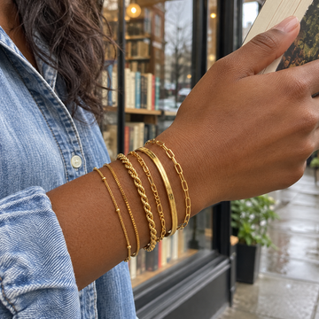 Gold six-chain bracelet stack on an adult wrist holding a book outside a shop · AI-generated illustrative demo image