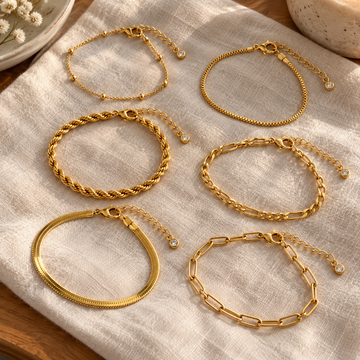 Six distinct gold bracelets arranged on cream linen with extender tails visible · AI-generated illustrative demo image