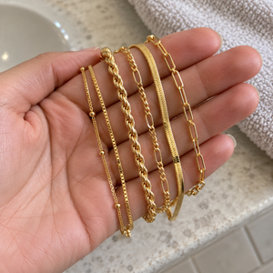 Six gold bracelet chains draped across an adult hand · AI-generated illustrative demo image