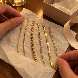 Six gold bracelet chains laid on tissue paper beside plain gift wrapping · AI-generated illustrative demo image